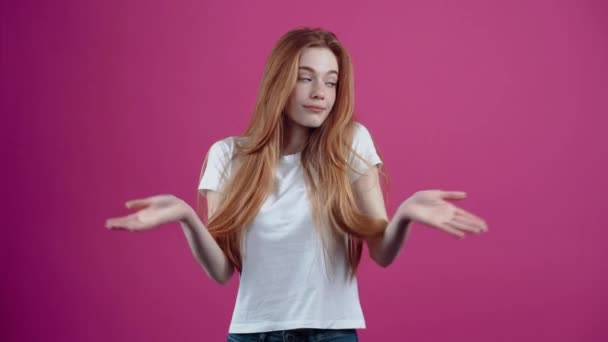 The portrait of a charismatic, ignorant girl shrugs and raises her hands in ignorance. Freckled teenage girl in a white T-shirt, isolated on a pink background. The concept of peoples lifestyle — Stock Video