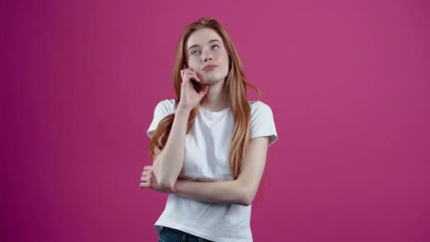 The charismatic teenager looked thoughtfully to one side with her hand on her chin. Freckled teenage girl in a white T-shirt, isolated on a pink background. The concept of peoples lifestyle — Stock Video