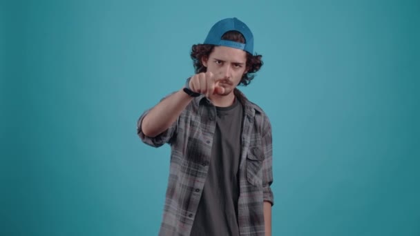 The charismatic young man with the cap, angrily calls someone, with his finger forward and a gesture of coming, puts his fist on his cheek and is ready to beat. isolated over turquoise background — Stock Video
