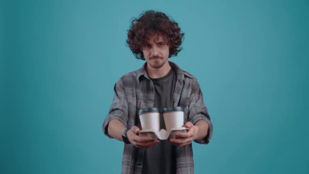 The thoughtful and cheerful student with 2 glasses of coffee in his hand calls his friends to have coffee. Isolated on a turquoise background. Concept of life. Peoples emotions. 4k portrait — Stock Video