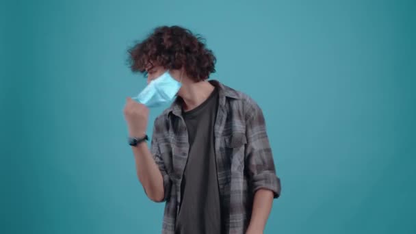 The charismatic and optimistic young man takes off his mask, raises his hands with joy and smiles broadly that he no longer needs to wear it, the pandemic is over. Isolated on a turquoise background — Stock Video