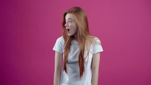 The portrait of a charismatic young woman looking to one side, sees something that makes her open her mouth in amazement and shows it to her friend. Freckled teenage girl in a white T-shirt, isolated — Stock Video