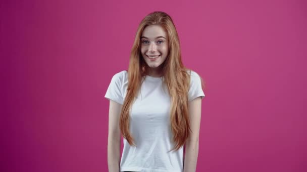 Porträttet av en lycklig flicka som försöker kväva lyckan med handflatorna i munnen. Fräknig tonåring flicka i en vit T-shirt, isolerad på en rosa bakgrund. Begreppet livsstil — Stockvideo