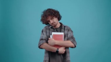 Karizmatik tebeşir gibi genç adam elinde birkaç kitap tutuyor ve işaret parmağını kafasına yerleştirerek okuma ihtiyacını vurguluyor. Turkuaz bir arka planda izole edilmiş. Hayat kavramı. İnsanlar