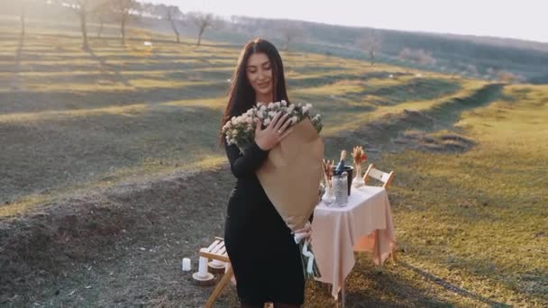 Den lyckliga kvinnan håller i sina armar en stor bukett blommor mottagna från sin pojkvän, isolerade i naturen, vid en romantisk middag i solnedgången — Stockvideo