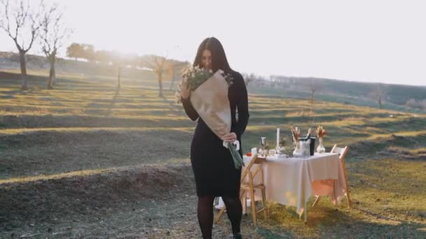Potret seorang wanita bahagia memegang karangan bunga besar dan berputar dengan antusias, di jantung alam dengan matahari terbenam, di makan malam romantis — Stok Video