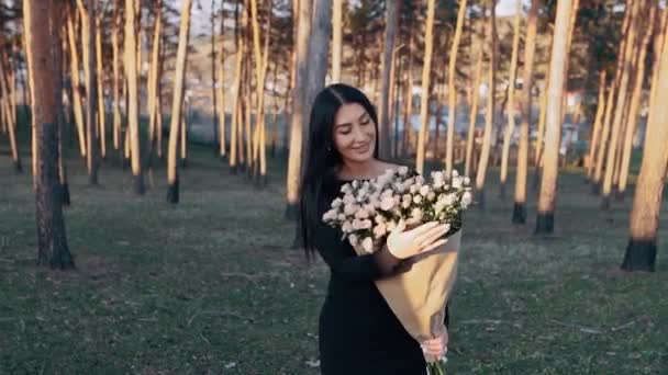 Potret seorang wanita muda karismatik di alam memegang karangan bunga indah di tangannya, dengan latar belakang matahari terbenam. Wanita muda yang baru saja dilamar — Stok Video