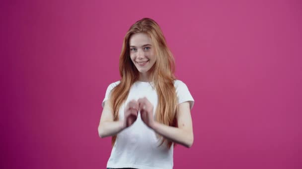 The charismatic and beautiful young woman shows her love by the sign of her heart taken to heart, playfully walks in front of him. Freckled teenage girl in a white T-shirt, isolated on a pink — Stock Video