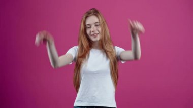 Ellerini tavşan kulağı gibi şakacı bir şekilde kafasına dayayan karizmatik bir genç kadının portresi. Beyaz tişörtlü, pembe arka planda izole edilmiş çilli genç kız. İnsanların konsepti