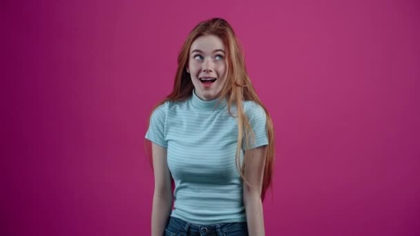 カリスマ的で楽観的で、ゆっくりと動く赤毛は、彼女がそれを好むという兆候で彼女の手を上げます。ピンクの背景に隔離された青いTシャツに身を包んだ10代の少女。人々の生活様式の概念 — ストック動画