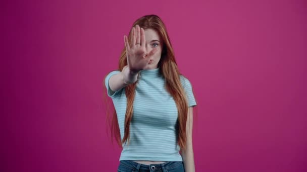 Stop. The pretty, serious young woman shows the stop sign and nods, no, no, no, crosses her hands in an x-shape. Freckled teenage girl in a blue T-shirt, isolated on a pink background. The concept of — Stock Video