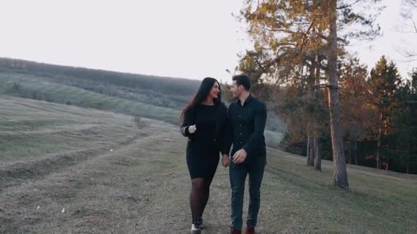 Unga par förälskade i naturen håller händer och ler, i slutet kramar den unge mannen sin flickvän och lyfter henne i sina armar — Stockvideo