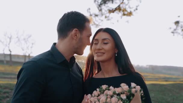 Los jóvenes felices se enamoran bajo el atardecer y se mantienen felices pegados entre sí. Ella lloró alegremente un gran ramo de flores, y él la miró enamorada. — Vídeos de Stock