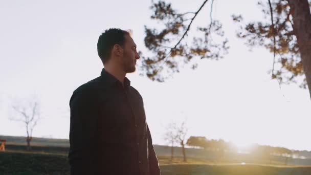 O homem sério e atencioso olha para o sol e, em seguida, vira a cabeça em partes, sendo relaxado pela beleza da natureza no pôr do sol — Vídeo de Stock