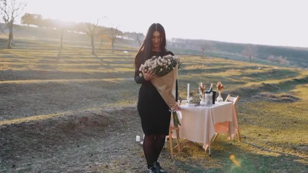 La jeune femme heureuse tient dans ses bras un grand bouquet de fleurs, dans le sein de la nature avec coucher de soleil, lors d'un dîner romantique — Video