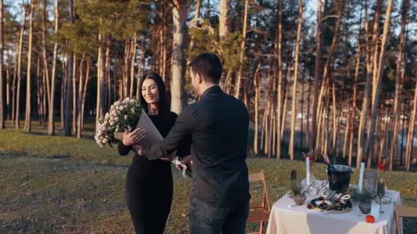 La giovane donna felice è sorpresa di ricevere un grande mazzo di fiori dal suo ragazzo e lo abbraccia amorevolmente, isolata nella natura, in una cena romantica sotto il tramonto. — Video Stock