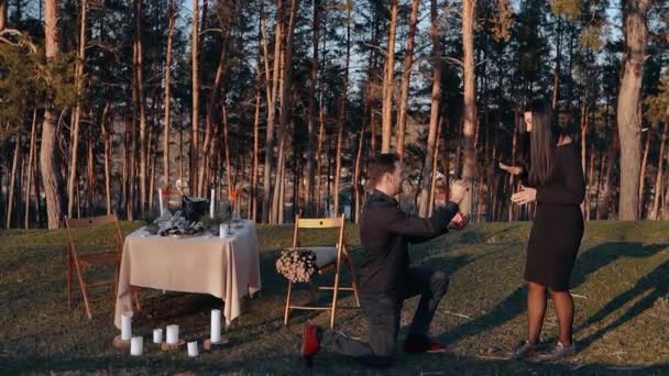 General setting with a young man who proposes in marriage his beloved in nature, against the background romantic decoration and fir trees. The young woman says yes — Stock Video