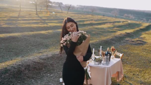 La jeune femme amoureuse sent bon le grand bouquet de fleurs reçu de son petit ami, dans le sein de la nature avec coucher de soleil, lors d'un dîner romantique — Video