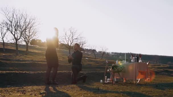 Isolated in nature, under the sunset, the man in love makes a marriage proposal to the beloved woman, on her knees, and she happily puts her hands to her mouth with joy — Stock Video