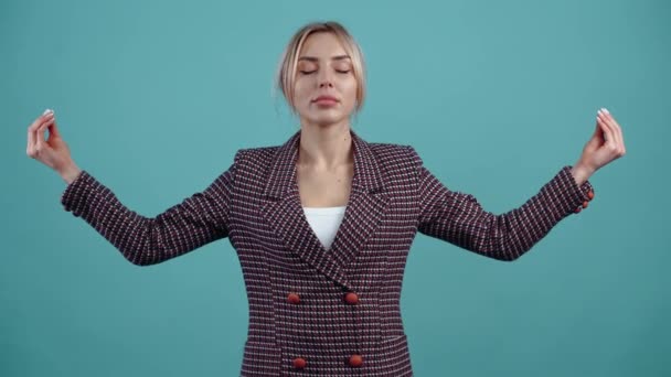 El retrato de una joven carismática meditando con las manos extendidas y los ojos cerrados, después de un momento de relajación muestra una sonrisa satisfecha. Aislada sobre un fondo turquesa. El concepto — Vídeo de stock