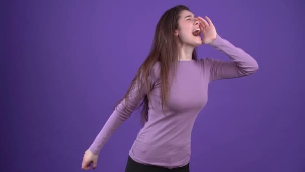 Panicked young woman, shouting loudly around for help. She is wearing a purple sweater in the studio on a purple background — Stock Video