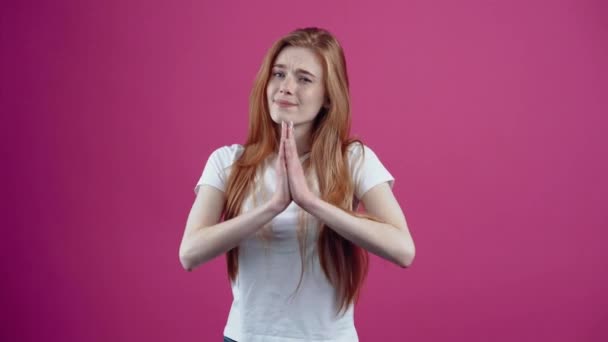 Por favor. Esperemos que la joven pelirroja junte sus manos en su pecho. Adolescente pecosa con una camiseta blanca, aislada sobre un fondo rosa. El concepto de estilo de vida de las personas. — Vídeos de Stock