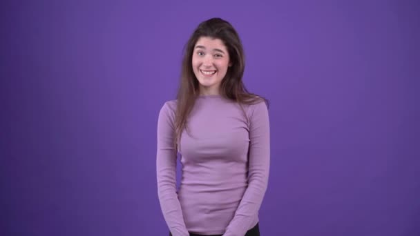 O retrato de uma bela jovem que é cética e faz seus olhos largos. Morena isolada em um fundo roxo, vestida com uma camisola roxa. Conceito de estilo de vida — Vídeo de Stock