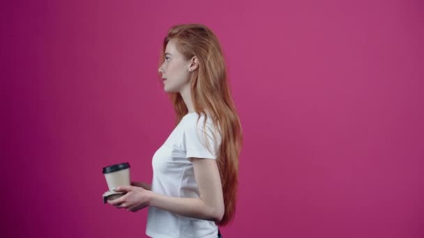 Харизматичная молодая женщина возвращается из профиля с двумя чашками кофе и раздает их, улыбаясь перед ней. Веснушчатый подросток в белой футболке, изолированный на розовом фоне. Концепция — стоковое видео