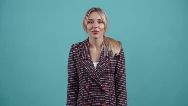 The blonde, amused by her blond hair, shows with her hand the gesture of a small size and displays small smiles. Isolated on a turquoise background. The concept of life. Peoples emotions. Portrait 4k — Stock Video