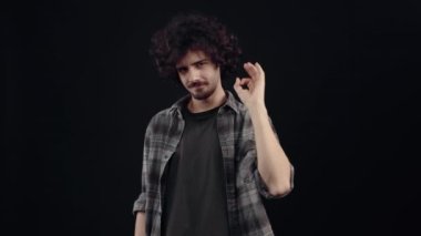 Kıvırcık saçlı karizmatik genç adam, tamam işaretini gösteriyor. Siyah arka planda izole edilmiş, yaşam kavramı. İnsanların duyguları işte. 4k portre