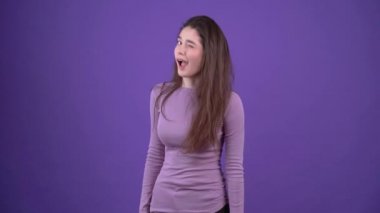 Karizmatik genç kadın komplocu gibi görünüyor ve elinde gizemli bir gülümseme gösteren bir işaret gösteriyor. Mor bir arka planda, mor bir kazak giymiş esmer kadın. Yaşam biçimi