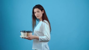 Doğal, karizmatik kız odaya geri döner ve elinde dört bardak kahveyle geniş bir gülümseme sergiler. Koyu saçlı Asyalı, mavi bluz giymiş, koyu mavi renkte izole edilmiş.