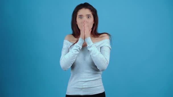 The frightened girl puts her palms to her lips and makes her eyes look shocked. Asian with dark hair, dressed in a blue blouse, isolated on a dark blue background in the studio. The lifestyle concept — Stock Video