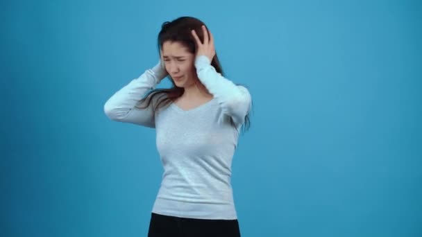 La joven irritada pone ambas manos sobre su cabeza y sacude sus manos en su cabello, agitando su cabeza. Asiático con el pelo oscuro, vestido con una blusa azul, aislado sobre un fondo azul oscuro en el — Vídeos de Stock