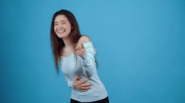 Elleri karnında ve işaret parmağı önceden belirtilmiş şekilde ağzı kulaklarına kadar gülen bir genç kadının portresi. Koyu renk saçlı Asyalı.