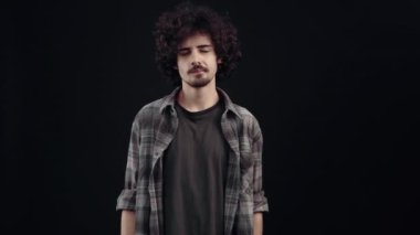 Düşünceli genç adam bakışlarını parçalar halinde hareket ettirir sonra işaret parmağını sessizliğe sokar ve sırrı saklar. Siyah arka planda izole edilmiş, yaşam kavramı. İnsanların duyguları işte. 4k portre