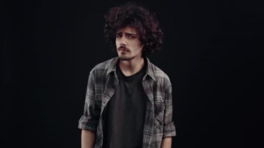 Kıvırcık, karizmatik, kafası karışık genç adam ona baktı, yüzünü buruşturdu ve hayır dedi, hayır, hayır, hayır. Siyah arka planda izole edilmiş, yaşam kavramı. İnsanların duyguları işte. 4k portre