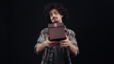 Gülümseyen utangaç bir çocuğun portresi, içinde hediye olan bir kutu taşıyor. Siyah arka planda izole edilmiş, yaşam kavramı. İnsanların duyguları işte. 4k portre