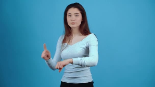 Le temps passe. La jeune femme sévère tape du doigt sur son poignet comme un signe que le temps est compté, retard. Asiatique aux cheveux foncés, vêtu d'un chemisier bleu, isolé sur un fond bleu foncé dans le studio — Video