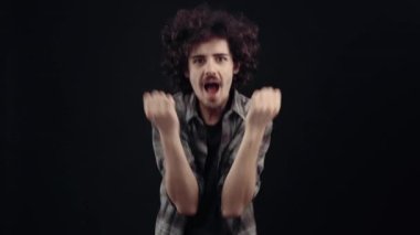 Yakışıklı ve kıvırcık genç adam haykırıyor ve hayret içinde ellerini kaldırıyor. Siyah arka planda izole edilmiş, yaşam kavramı. İnsanların duyguları işte. 4k portre