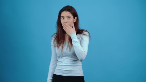 Het portret van een verbaasd meisje die haar hand op haar mond legt om haar te bedekken. Aziatisch met donker haar, gekleed in een blauwe blouse, geïsoleerd op een donkerblauwe achtergrond in de studio. Het levensstijl concept — Stockvideo