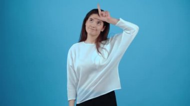 Kız, kaybeden işareti altında elini alnına koyar ve şakacı bir şekilde başını sallar. Koyu saçlı, mavi bluz giymiş, stüdyoda koyu mavi bir arka planda izole edilmiş bir Asyalı. Şey...