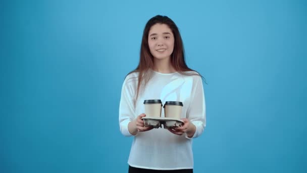 A jovem mulher sorrindo espalha quatro copos de café colocados em um suporte. Asiático com cabelo escuro, vestido com uma blusa azul, isolado em um fundo azul escuro no estúdio. O conceito de estilo de vida — Vídeo de Stock