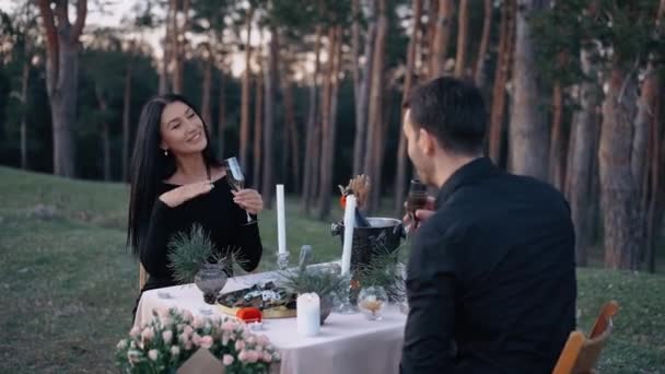 La pareja enamorada cena en la naturaleza, a la luz del sol abrasador. Celebra el compromiso con una copa de champán. Concepto de estilo de vida de los amantes jóvenes — Vídeos de Stock