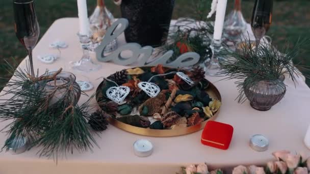 The close up of the decorative table on which is a plate with natural elements, including pine cones, others are positioned candles and a love element — Stock Video