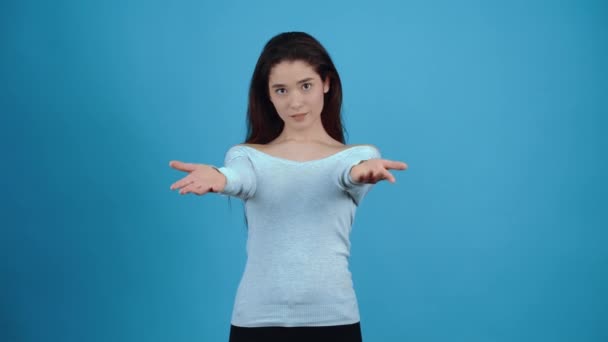 Portrættet af en pige, der viser et opkald med hænderne, kom til mig for et knus. Asiatisk med mørkt hår, klædt i en blå bluse, isoleret på en mørkeblå baggrund i studiet. Livsstilsbegrebet – Stock-video