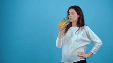 Mutlu kız pipetle bir bardak meyve suyundan içer, mutlu bir şekilde nefes alır ve mutlu bir şekilde içer. Koyu saçlı, mavi bluz giymiş koyu mavi arka planda izole edilmiş bir Asyalı.