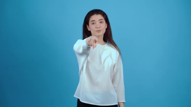 The disappointed, mischievous young woman points with her index finger forward and points with her other hand at the loser. Asian with dark hair, dressed in a blue blouse, isolated on a dark blue — Stock Video