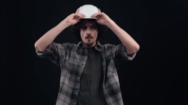 Karizmatik hippi çocuk mühendis kaskını takar ve gururla kameraya bakar. Siyah arka planda izole edilmiş. Hayat kavramı. İnsanların duyguları işte. 4k portre