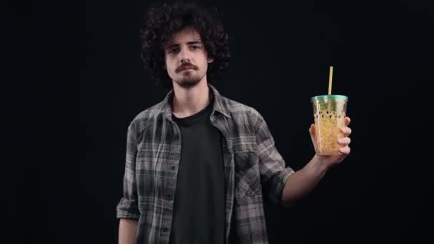 The charismatic young man holds a straw glass in one hand, points to him, satisfied and smiling, puts his hand on his belly, and then shows the like sign. Isolated on black background. The concept of — Stock Video